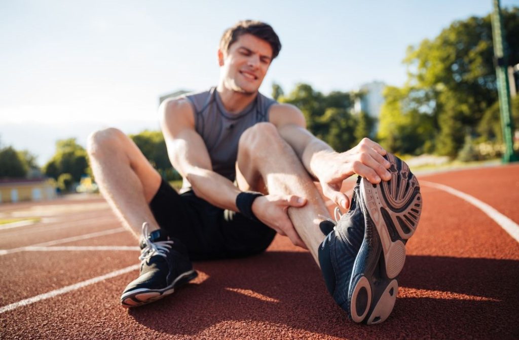 Jogger sitzt auf Aschenbahn und simuliert einen Krampf wegen Magnesium Mangel