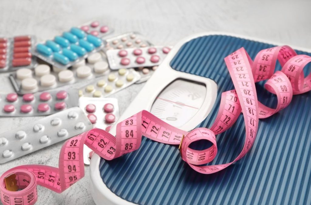 viele Tabletten zum Abnehmen neben einer Waage und Maßband