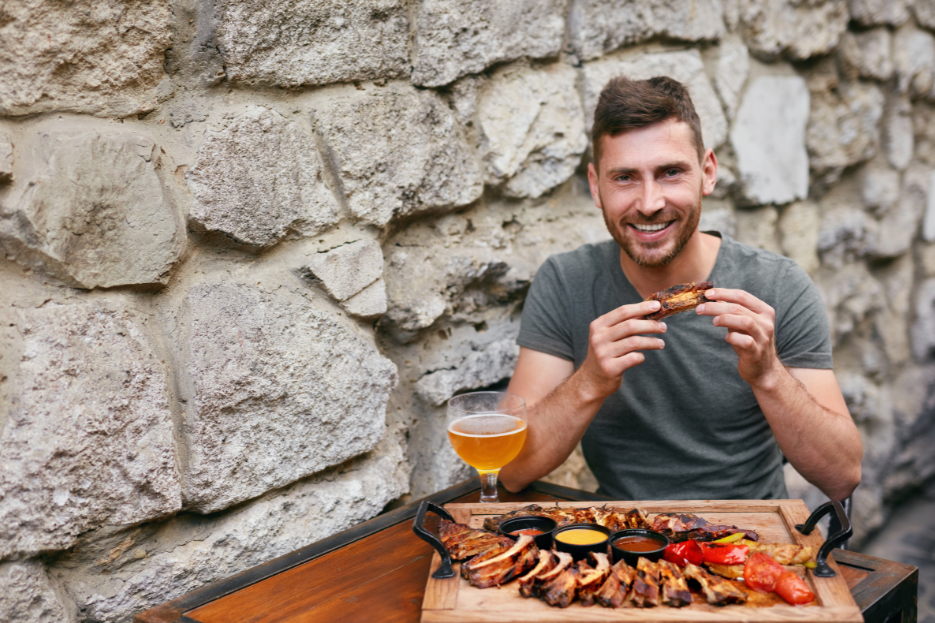 Mann isst Grillfleisch vor Steinwand symbolisch für Paleo Steinzeitdiät
