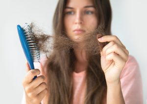 Haarausfall durch Vitaminmangel dargestellt von junger Frau mit Bürste