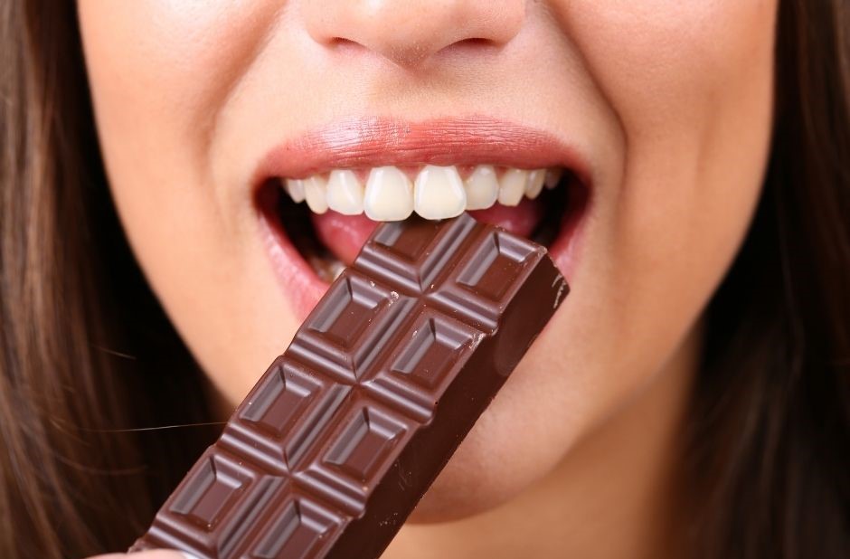 Heißhungerattacken können durch dunkle Schokolade verhindert werden, dargestellt von Frau mit Tafel Schoko