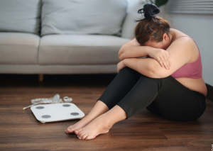 Abnehmen erschwert durch negatives Mindset symbolisiert von gefrusteter Frau neben Waage