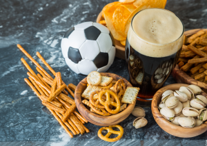 Bierbauch durch ungesunde Snacks: Bier, Chips, Salzstangen und ein kleiner Fußball runden das Bild ab