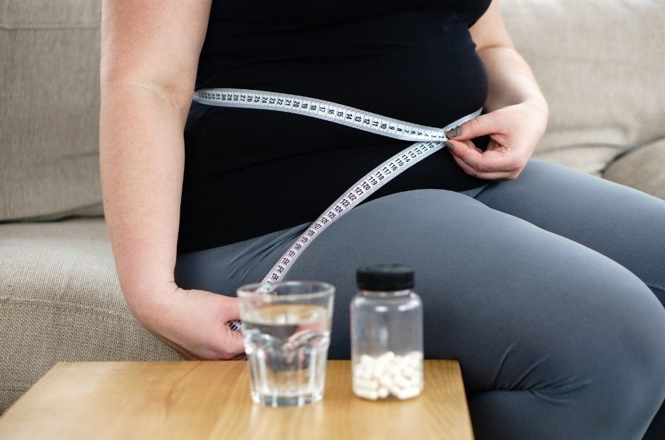 Verhindern Hormone Abnehmen dargestellt von adipöser Frau mit Pillen und Wasserglas