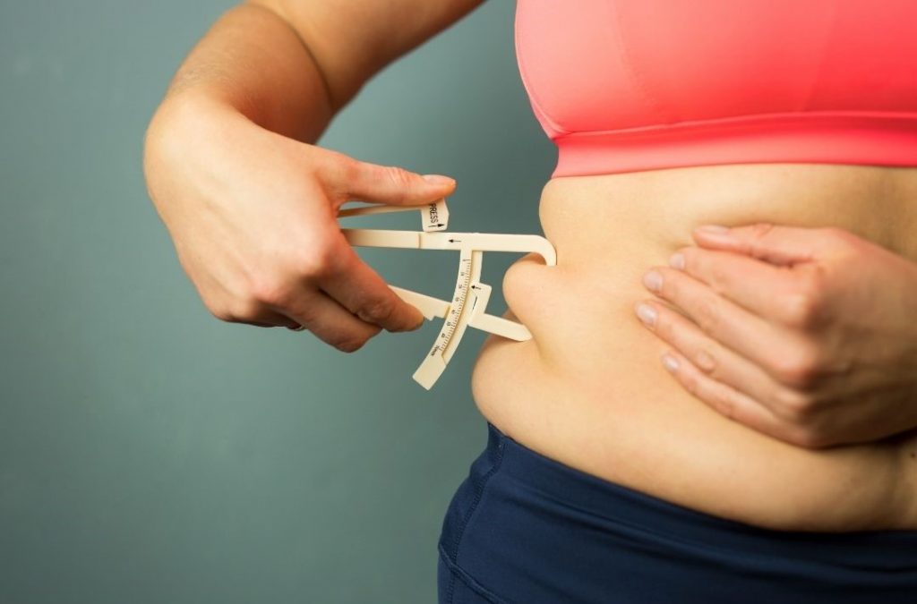 Kaloriendefizit dargestellt von Frau bei Hautfaltenmessung an der Hüfte