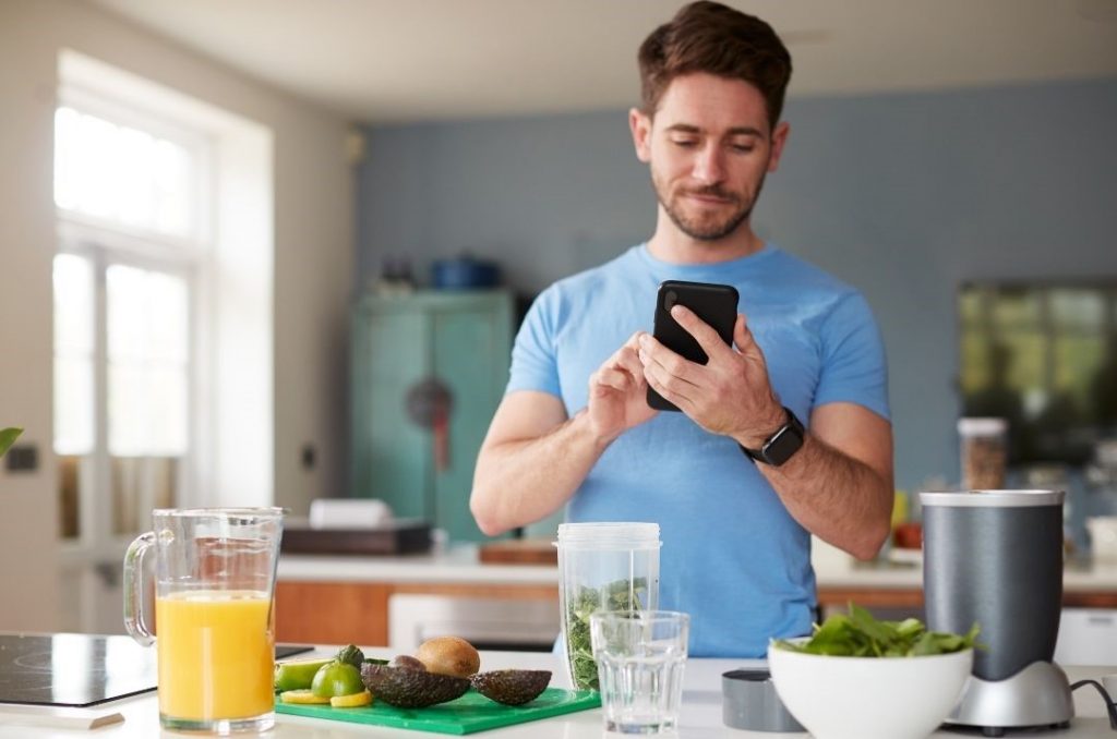 Kaloriendefizit dargestellt von Mann in Küche beim Kalorien Tracking mit Handy